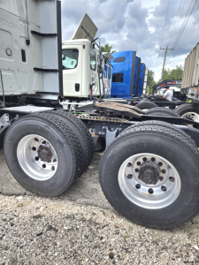Dual-wheel tractor truck chassis showing rear axles and tires with fifth wheel and cab in background.