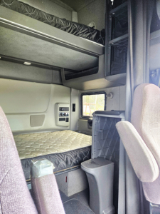 Interior of a used 2020 International condo sleeper showing a lower bunk and upper bunk, side storage, and captain chair in the cab.