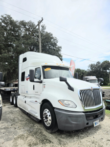 Truck cab showing International CONDO sleeper with double bunk, white exterior, grille, and front bumper; dealership lot in background.