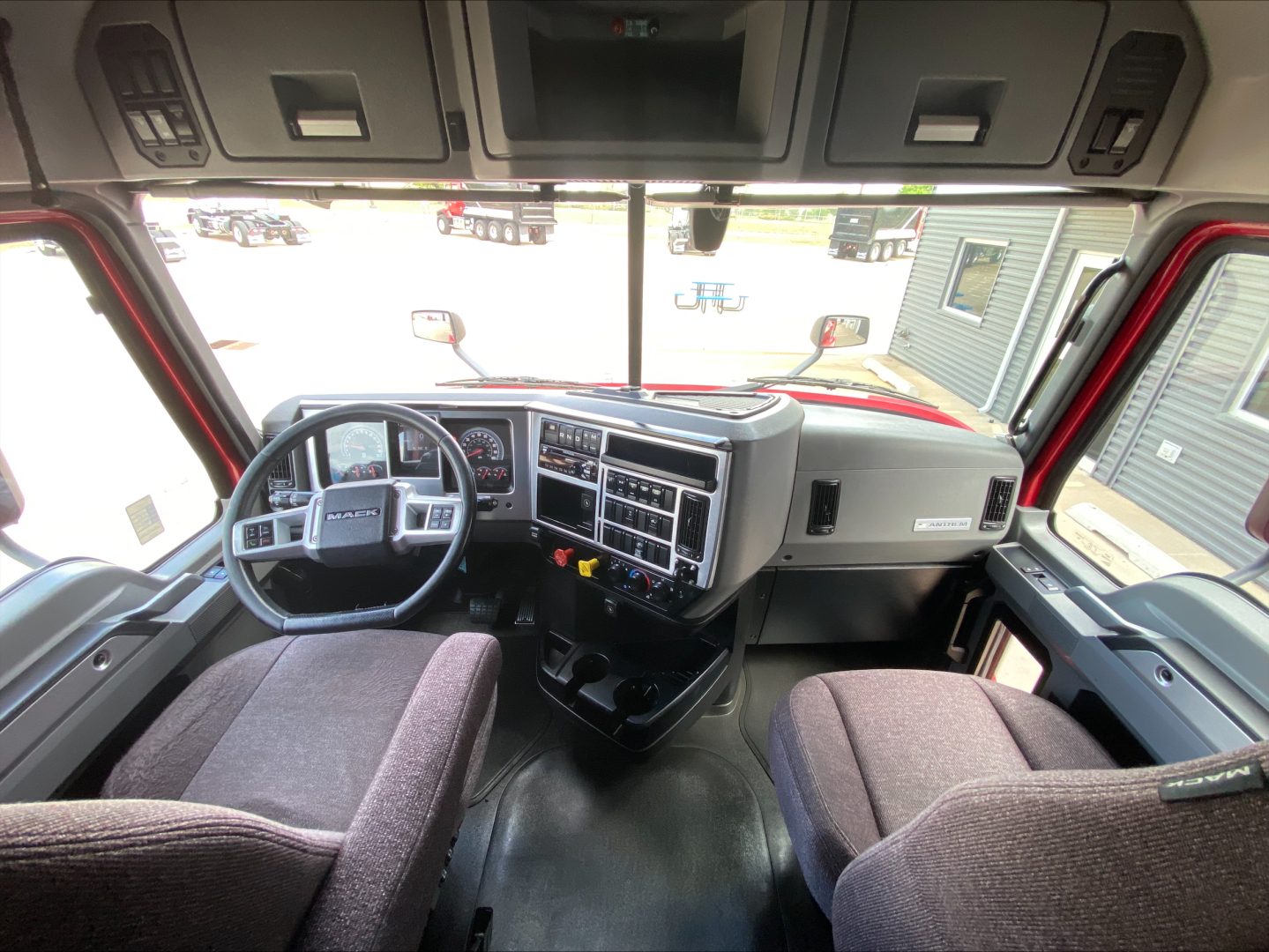 Truck cabin interior showing steering wheel, dashboard with numerous gauges, center console, and two front seats. Visible on dash: various controls and vents.
