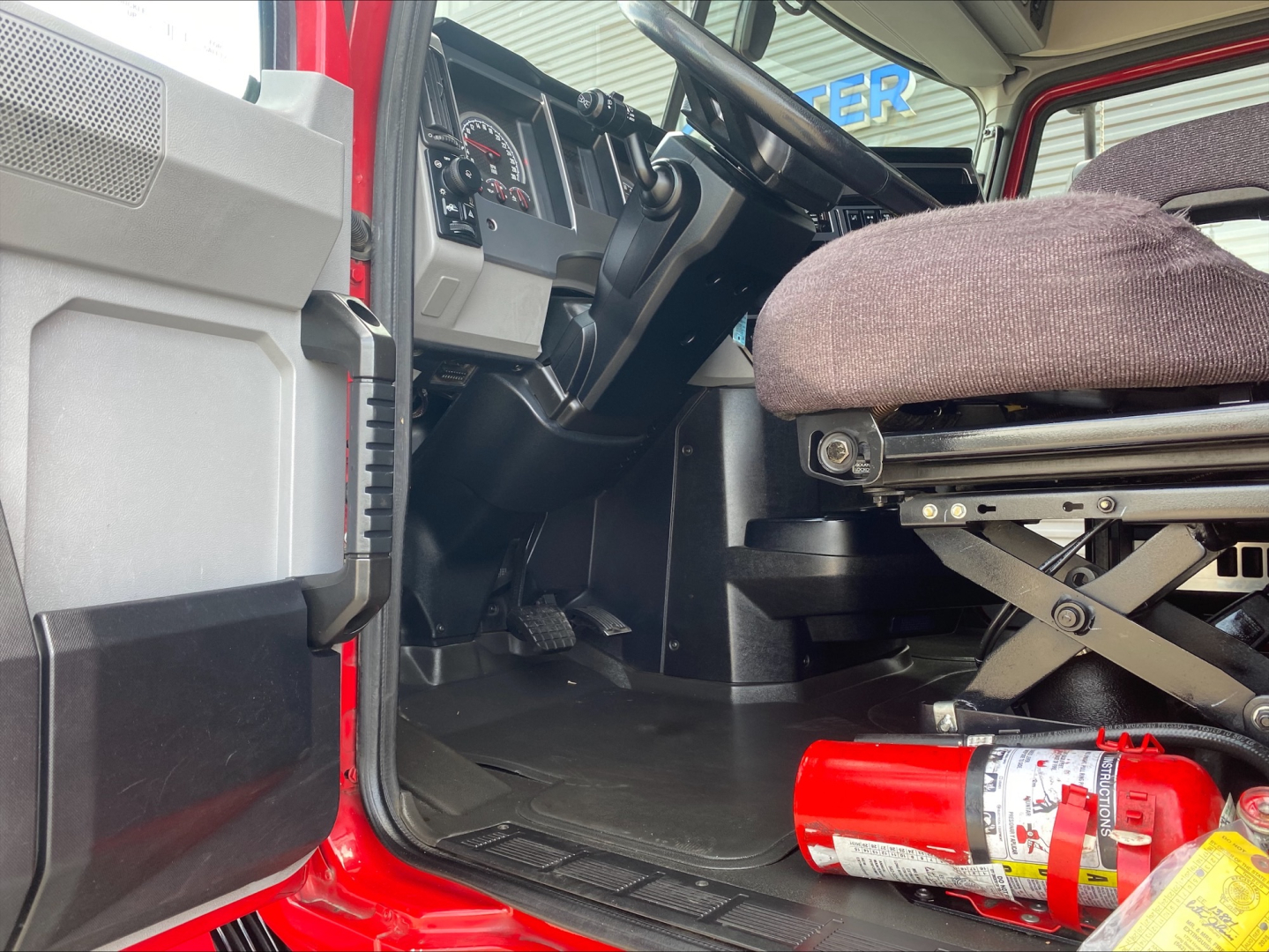 Truck cabin interior of a 2020 Mack AN64T70 from the driver's side showing steering wheel, dash, and grey/black interior with a red fire extinguisher on the floor.