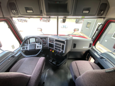 Truck cabin interior showing steering wheel, dashboard with numerous gauges, center console, and two front seats. Visible on dash: various controls and vents.
