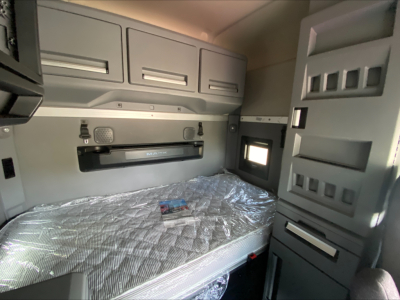 Truck cab interior showing sleeper berth with overhead cabinets and window, image from a 2020 Mack AN64T70 listing.