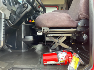 Cab interior of a 2020 Mack AN64T70 showing driver seat base, steering column, accelerator/brake area, and a red fire extinguisher on the floor.