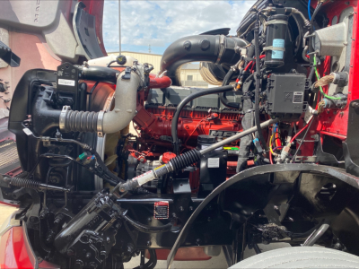 Mack AN64T70 truck engine bay with red engine block, exposed hoses, and surrounding components.