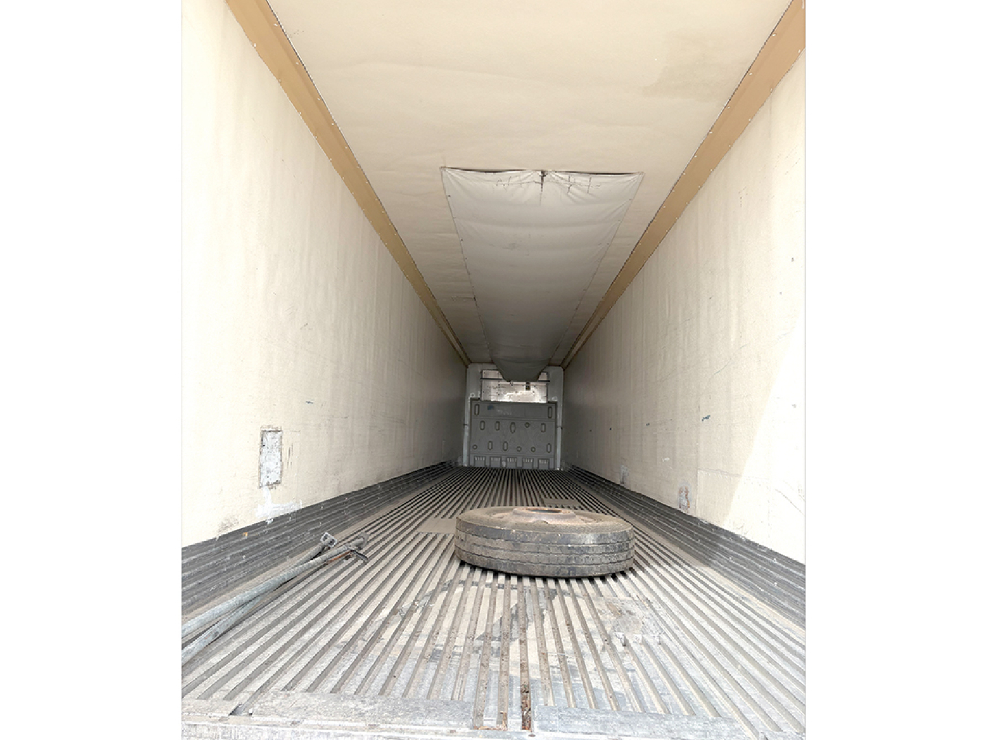 Trailer cargo area interior showing a spare tire lying on ribbed floor and rear hatch in background.