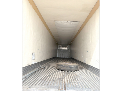 Trailer cargo area interior showing a spare tire lying on ribbed floor and rear hatch in background.