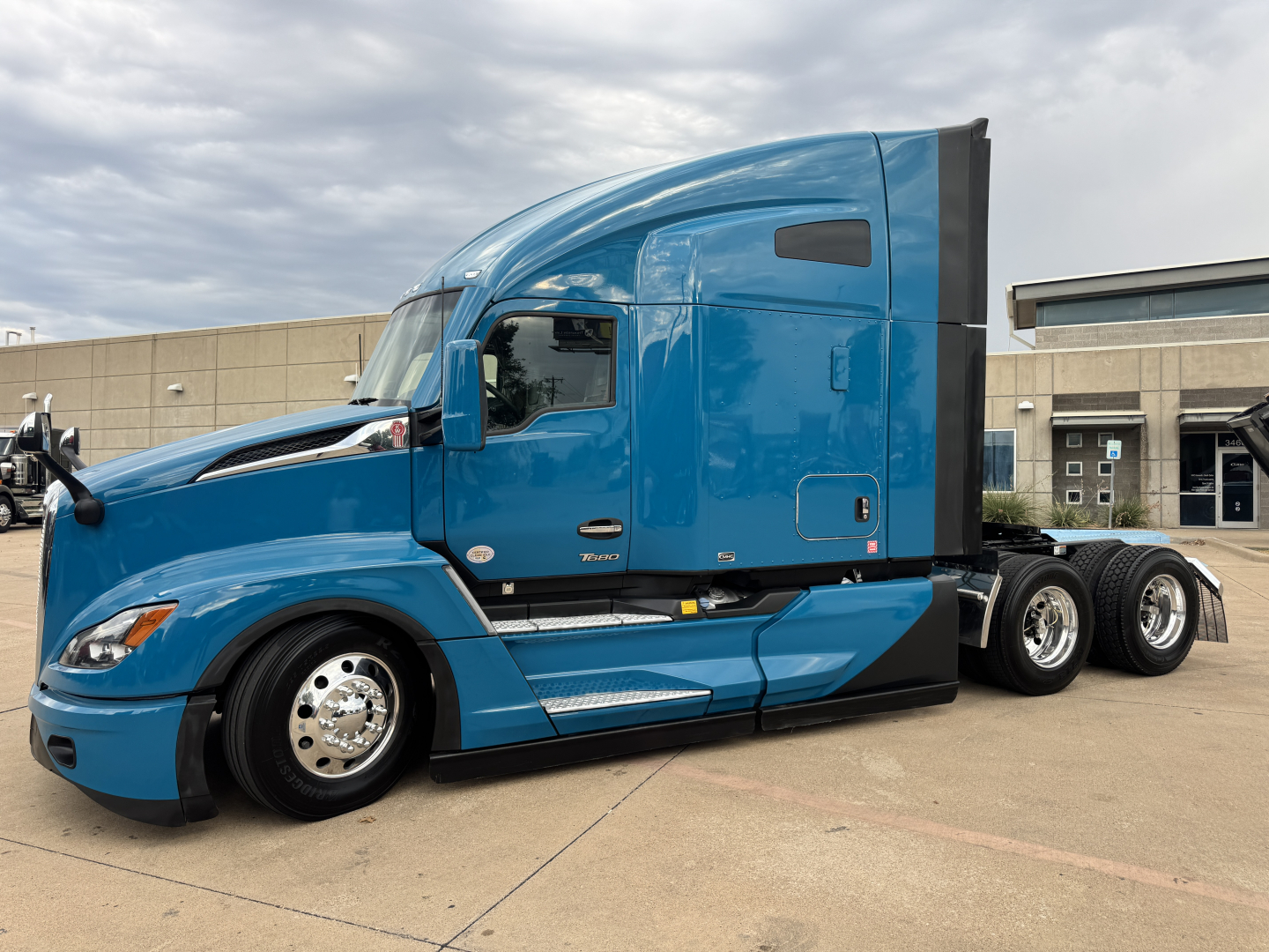 Kenworth T680 tractor-trailer in blue, side view showing sleeper cab and rear wheels