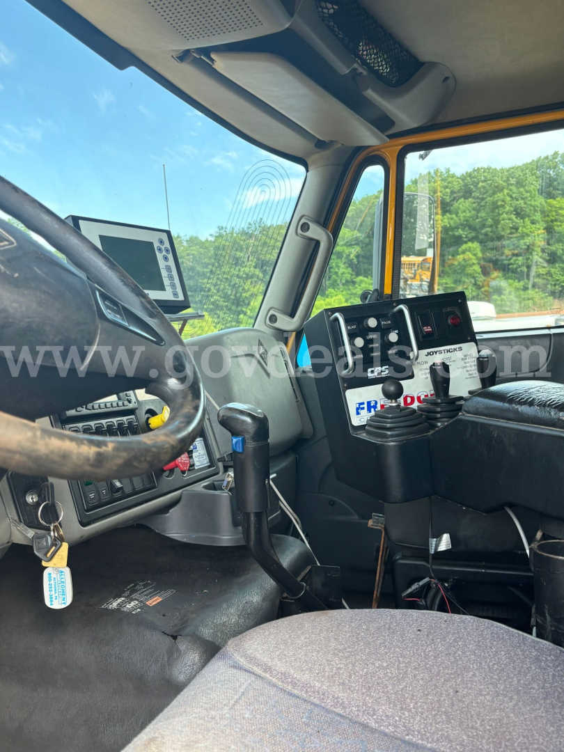 Cab interior of a 2011 International 7600 dump truck showing steering wheel, control panels, and dashboard with multiple gauges and gear levers.