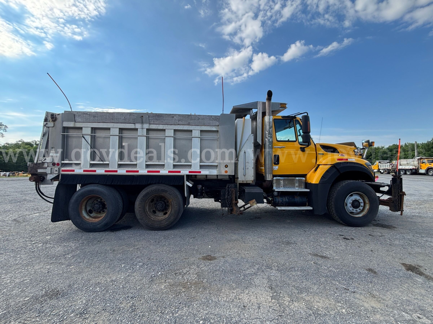 Dump truck side view showing a yellow International 7600 with a gray dump bed in a used equipment lot.