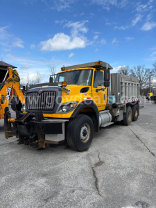 Dump truck showing 2011 International 7600 dump truck in yellow with black grille, front bumper guard, and dump bed; stock number 30360 visible.