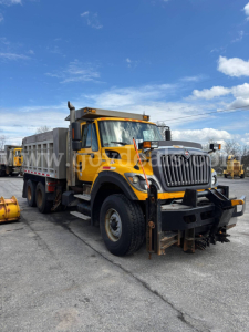 Dump truck with yellow cab and gray dump bed, front view in lot