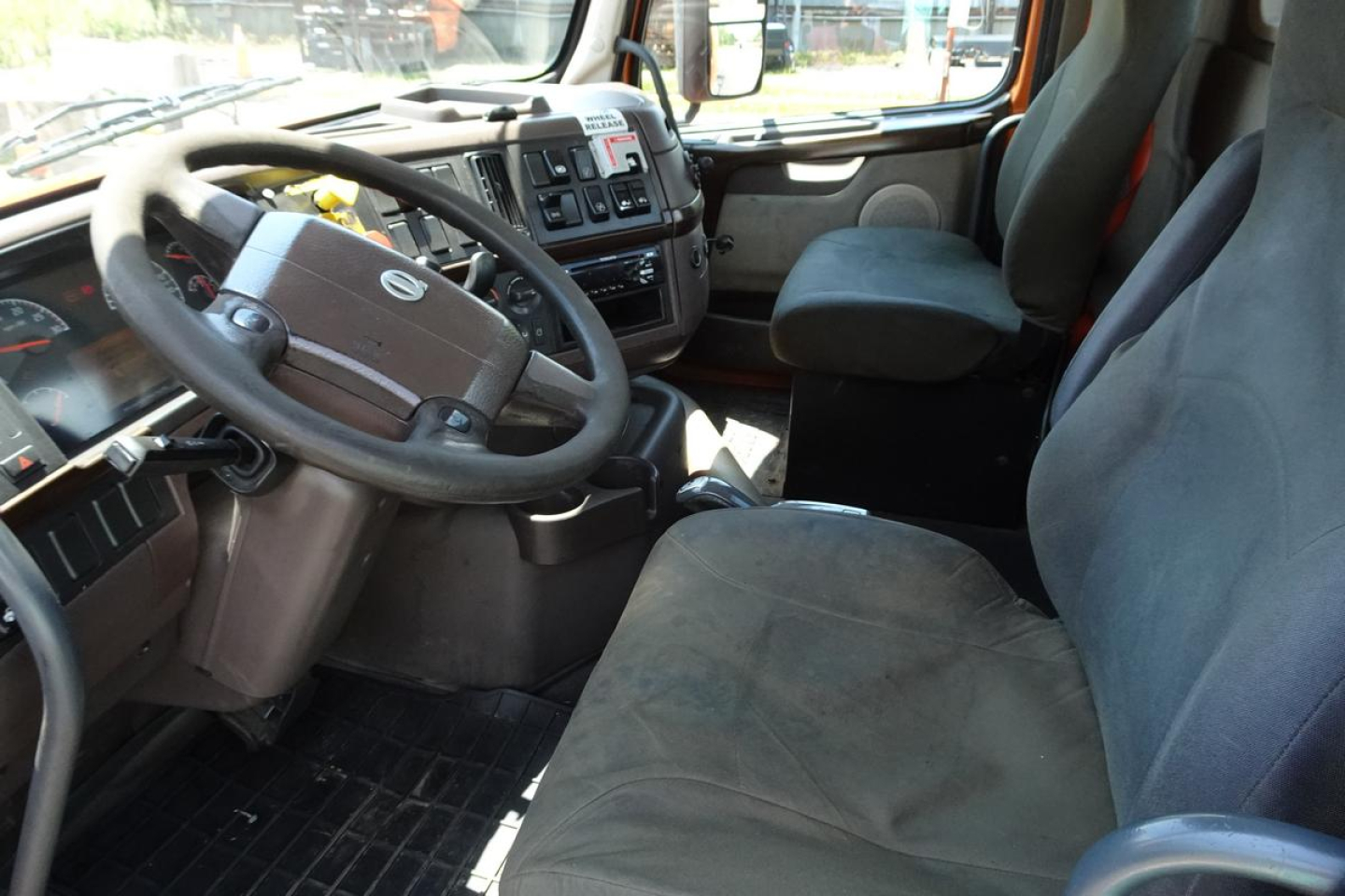 Interior of a Volvo VNM64T truck cab showing steering wheel and dashboard, with driver and passenger seats visible.
