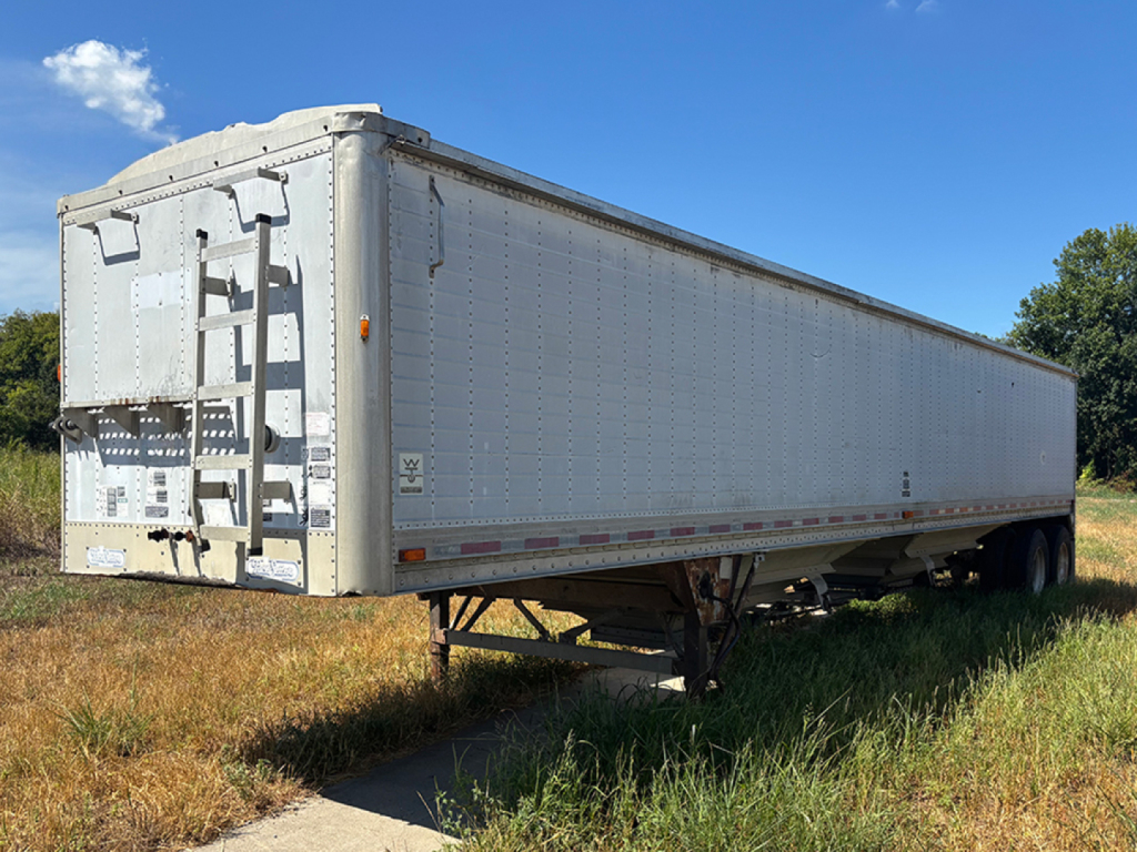 Trailer side view showing a long white hopper trailer with a platform ladder at the rear and dual axle undercarriage.