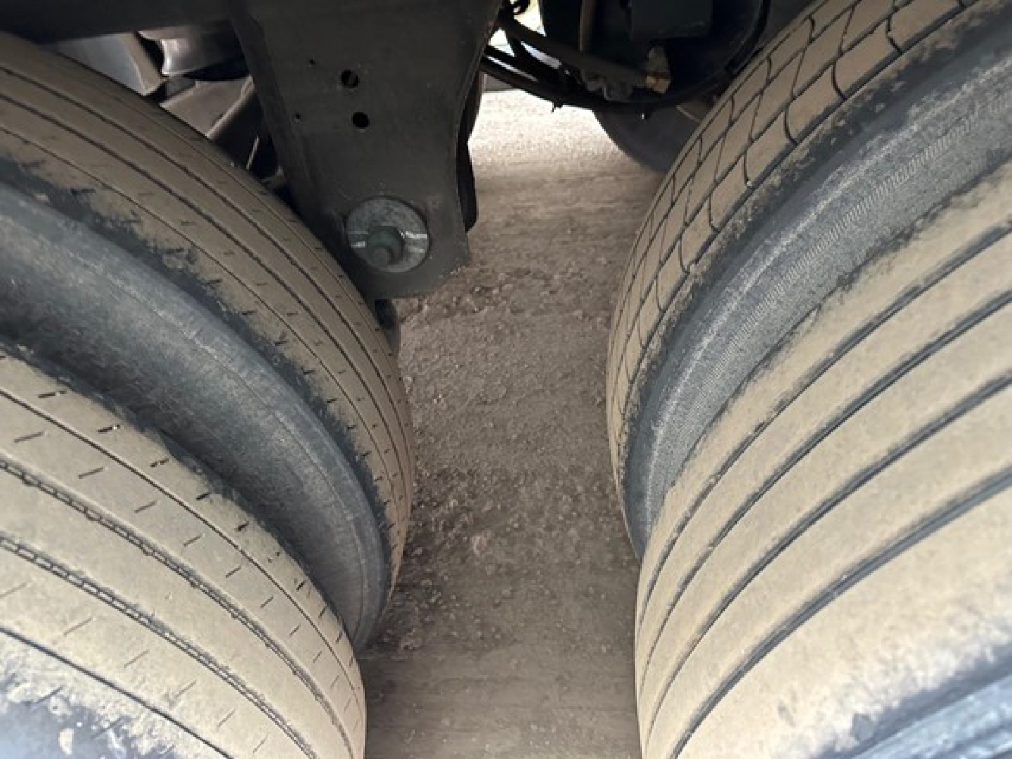 Trailer axle end showing dual tires and suspension mount with the frame and bolt.