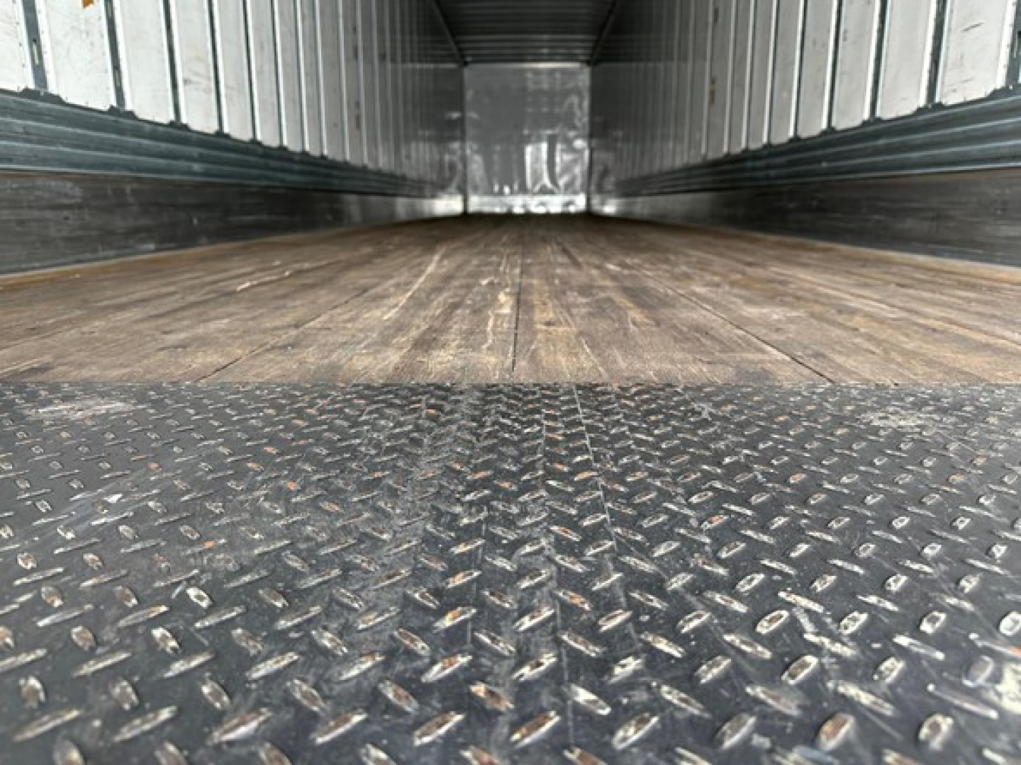 Trailer interior showing wood floor and diamond plate metal threshold with side rails and ceiling; empty cargo space.