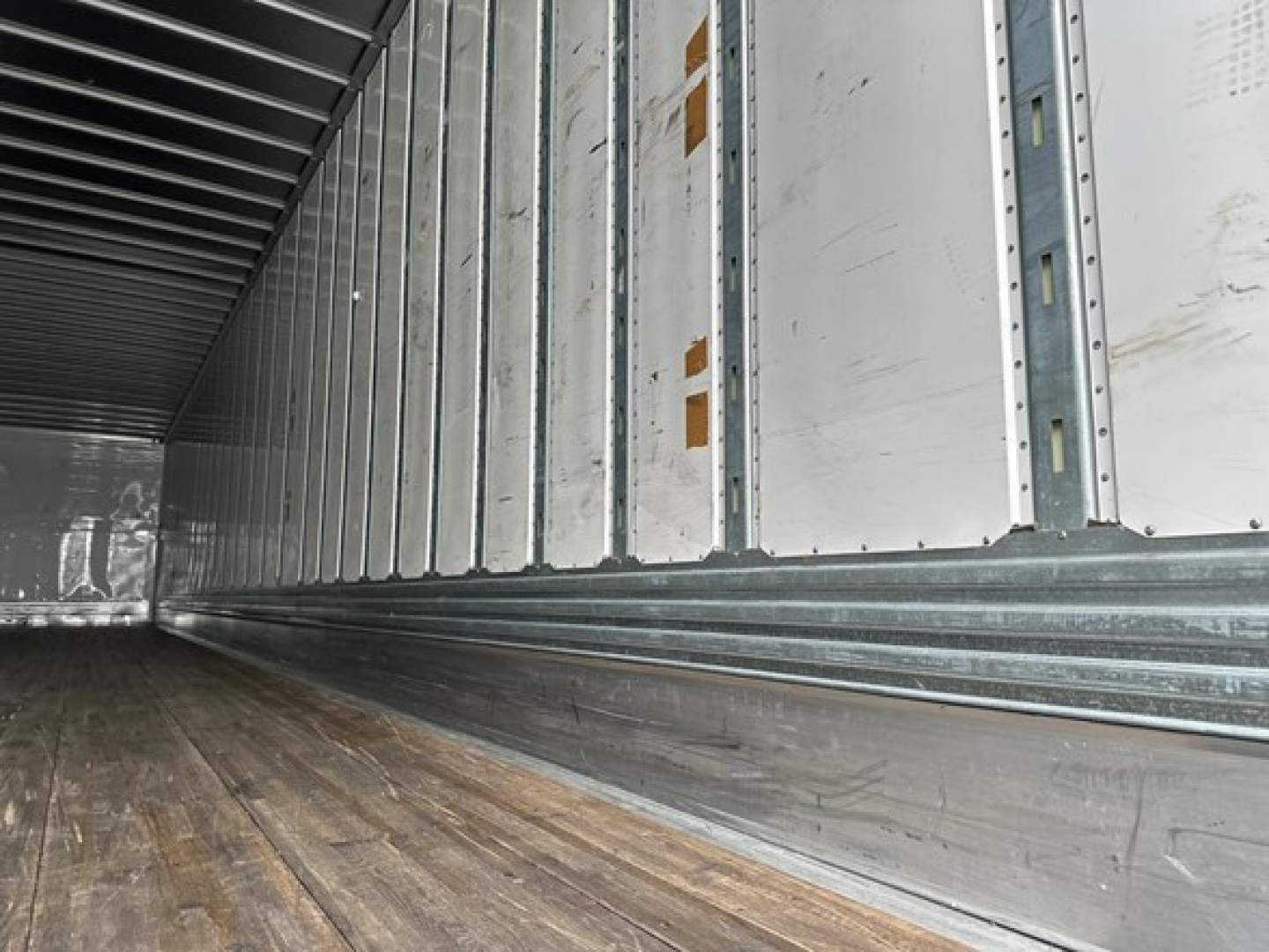 Trailer interior showing metal side walls and wooden floor, long cargo space with ribbed ceiling beams.