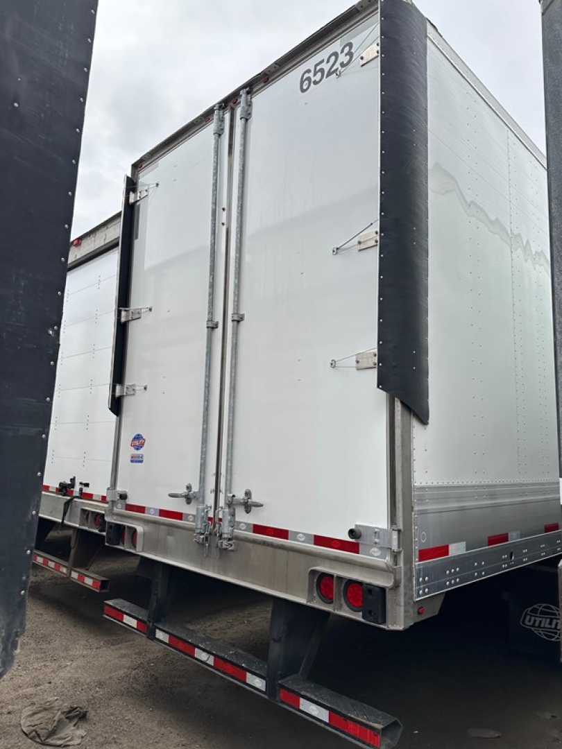 Trailer rear view showing double rear doors, silver aluminum body, black corner protectors, red and white reflective tape, and taillights.