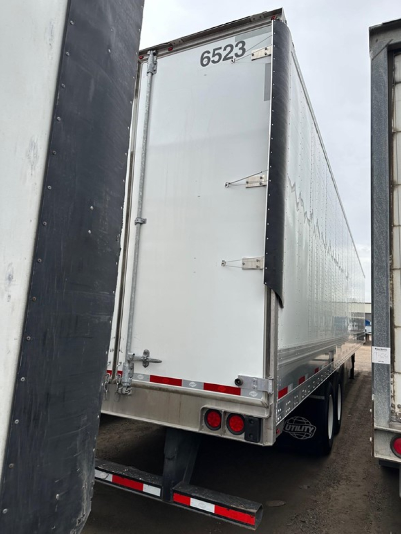Utility 4000dx trailer rear view showing numeric id 6523 on top, dual rear lights, white back door, and side panels; visible bumper and wheels.