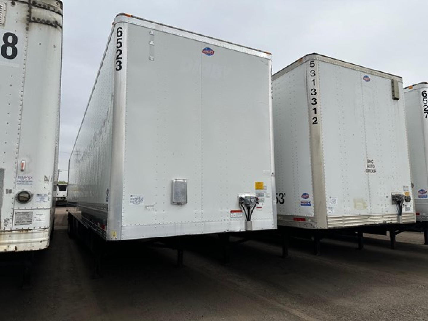 Trailer in a lot showing a white utility box van/trailer with rear doors, numbers on sides, and wheel-less bottom undercarriage visible.