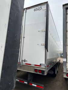 Utility 4000dx trailer rear view showing numeric id 6523 on top, dual rear lights, white back door, and side panels; visible bumper and wheels.