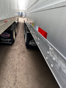 Trailer sides of Utility 4000DX show aluminum panels, riveted seams, and red/white reflective markings between two trailers in a narrow alley.