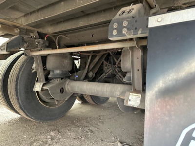 Trailer undercarriage showing axle, leaf springs, and dual wheels with label sticker, view from beneath utility trailer.