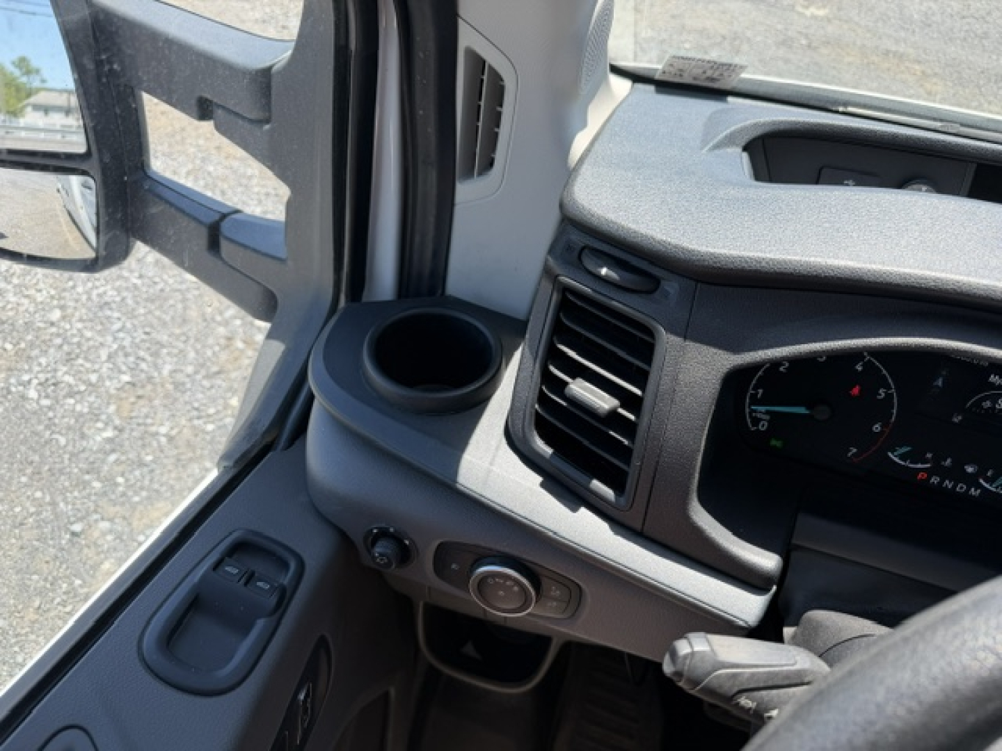 Ford Transit 350HD interior dash area with steering wheel, HVAC vent, cup holder, and control knob near door; partial instrument cluster visible
