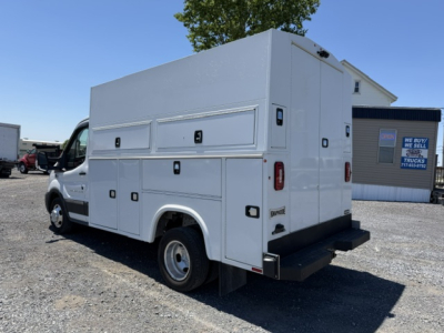 Ford Transit 350HD service/body truck with utility compartments on the sides and rear doors, white utility cargo box on chassis, no visible text other than stickers on doors.