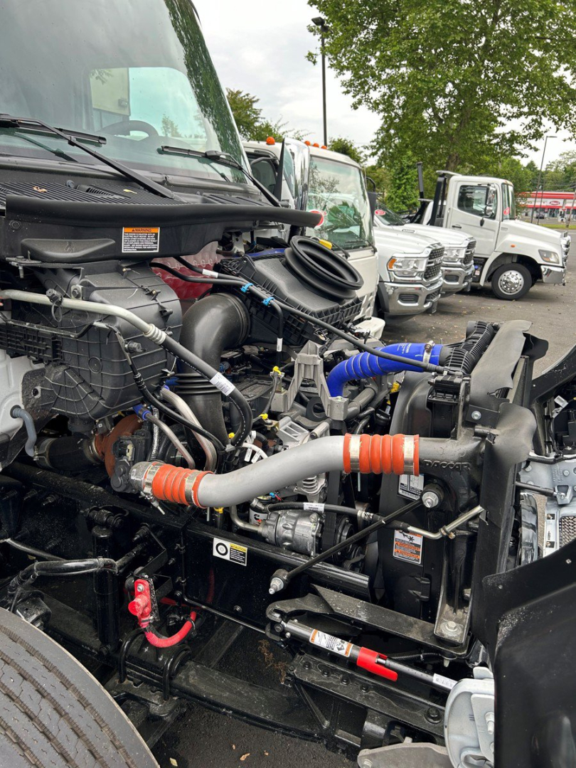 Kenworth T280 engine bay view showing intake hoses, coolant reservoir, and various hydraulic lines near the front. Visible components include hoses with orange and blue couplers, radiator, and surrounding engine bay hardware.