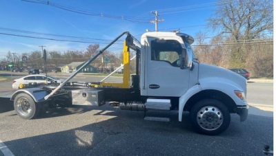 Kenworth T280 hooklift truck side view showing loading arms and cab with metallic silver body and yellow hooklift.