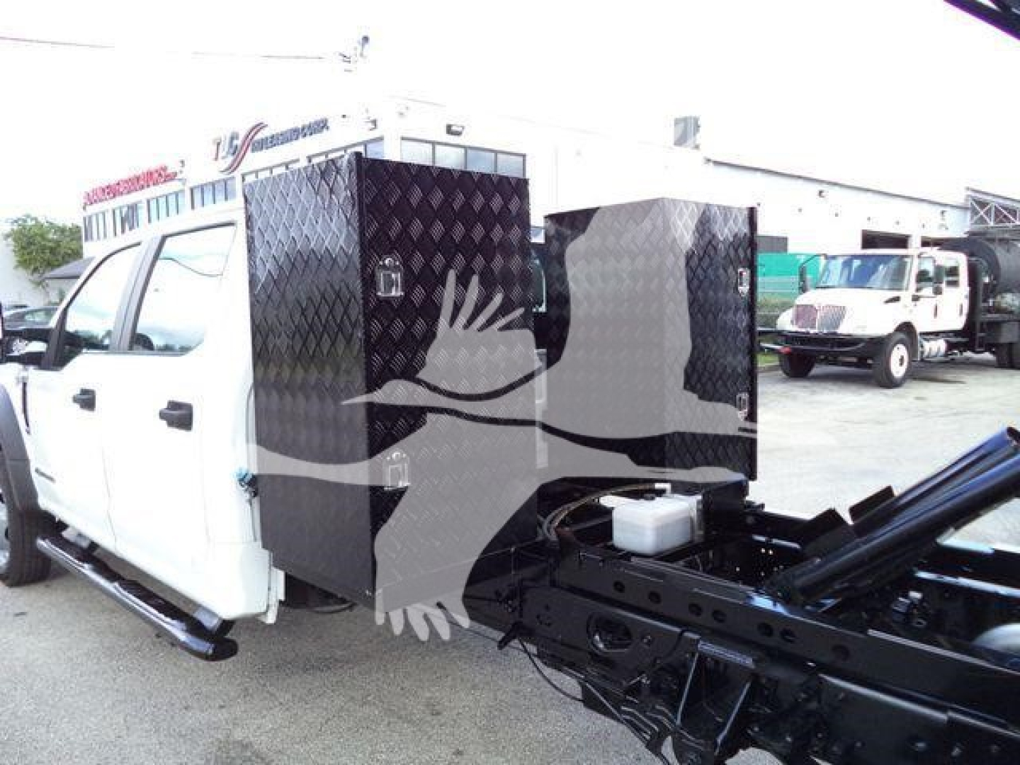Dump truck chassis with diamond-plate toolboxes mounted behind cab; white Ford F-550XL cab, black chassis frame, hydraulic components visible.