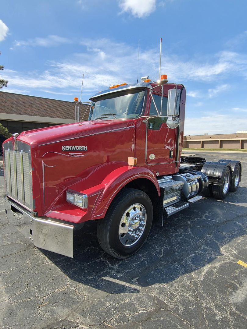 Kenworth T800 conventional daycab truck showing front grille and left side, red paint, chrome bumper, dual rear axles, with Kenworth emblem