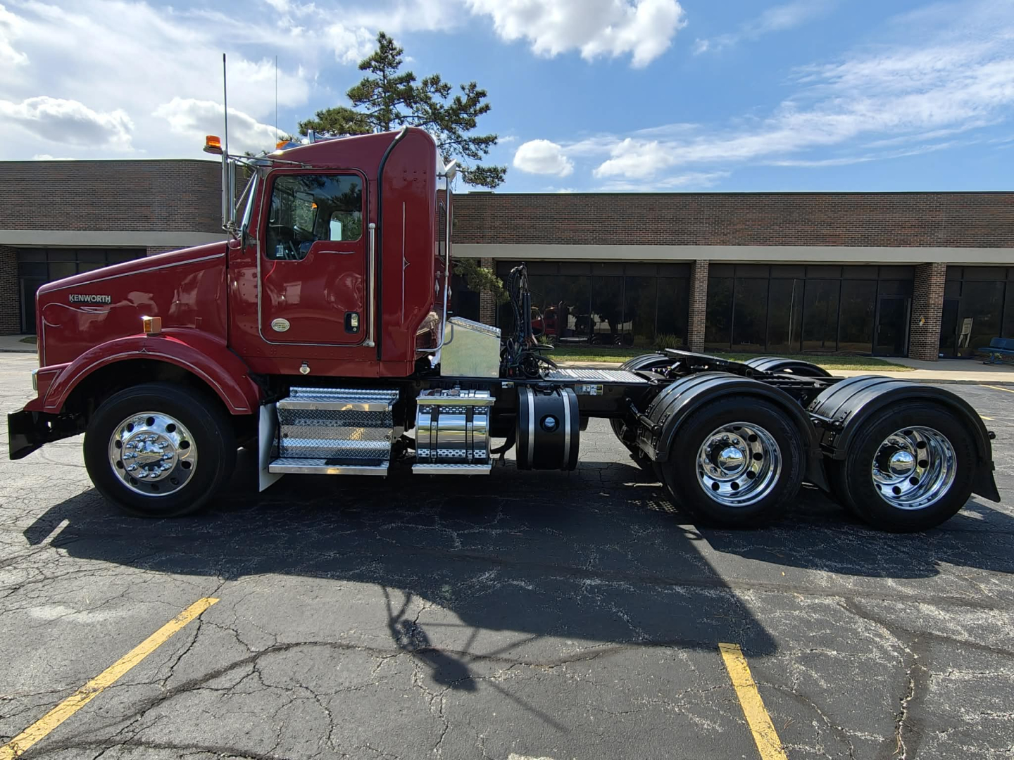 Kenworth T800 conventional daycab truck side view showing red cab and chassis with dual rear axles and chrome fuel tanks.