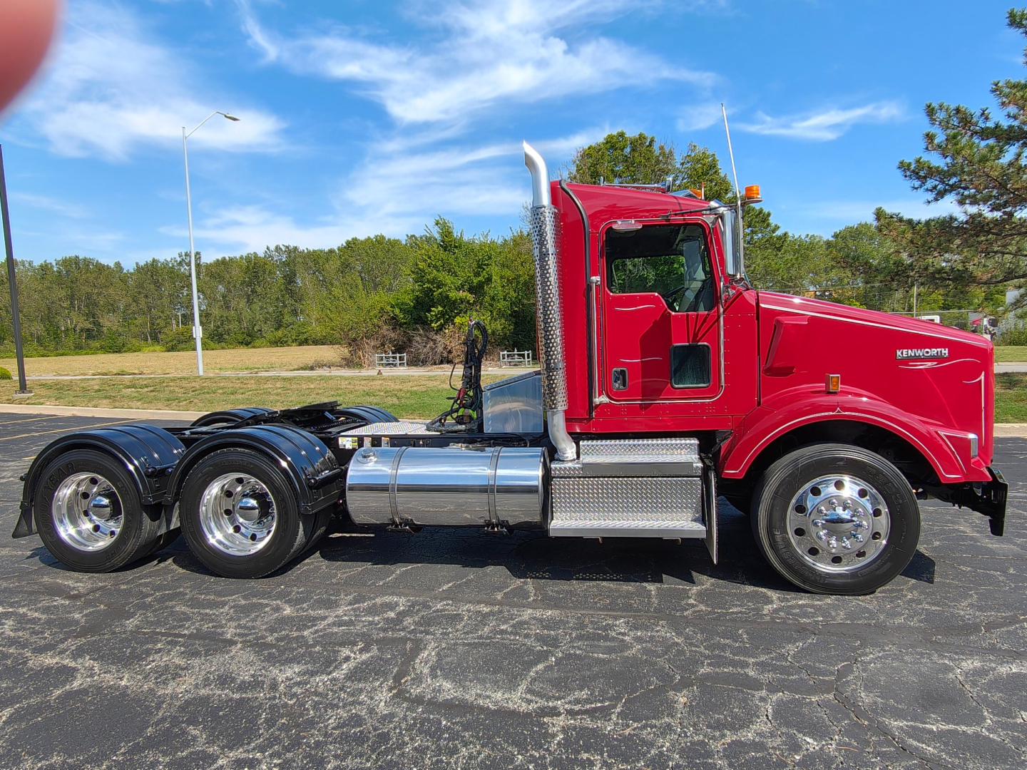 Kenworth T800 tractor in red cab side view showing chrome exhaust stack and fuel tanks, tri-axle rear with polished wheels.