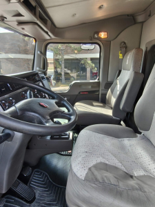 Cab interior of 2020 Kenworth T800 truck showing steering wheel, driver seat, passenger seat, dashboard, and door with window; view through windshield and side window.