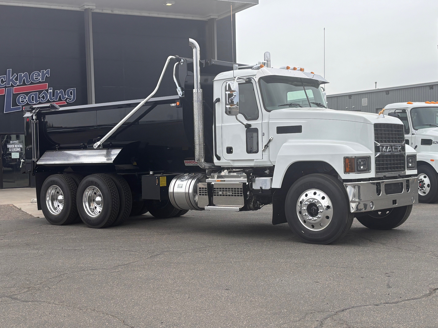 2026 Mack PI64 dump truck side view showing dump bed and chassis with dual rear axles and white cab.