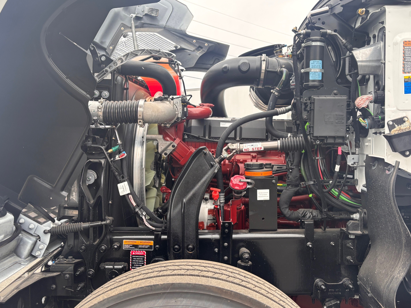 Mack PI64 engine bay showing red engine components, hoses, wiring, and fluid reservoirs visible in the compartment.