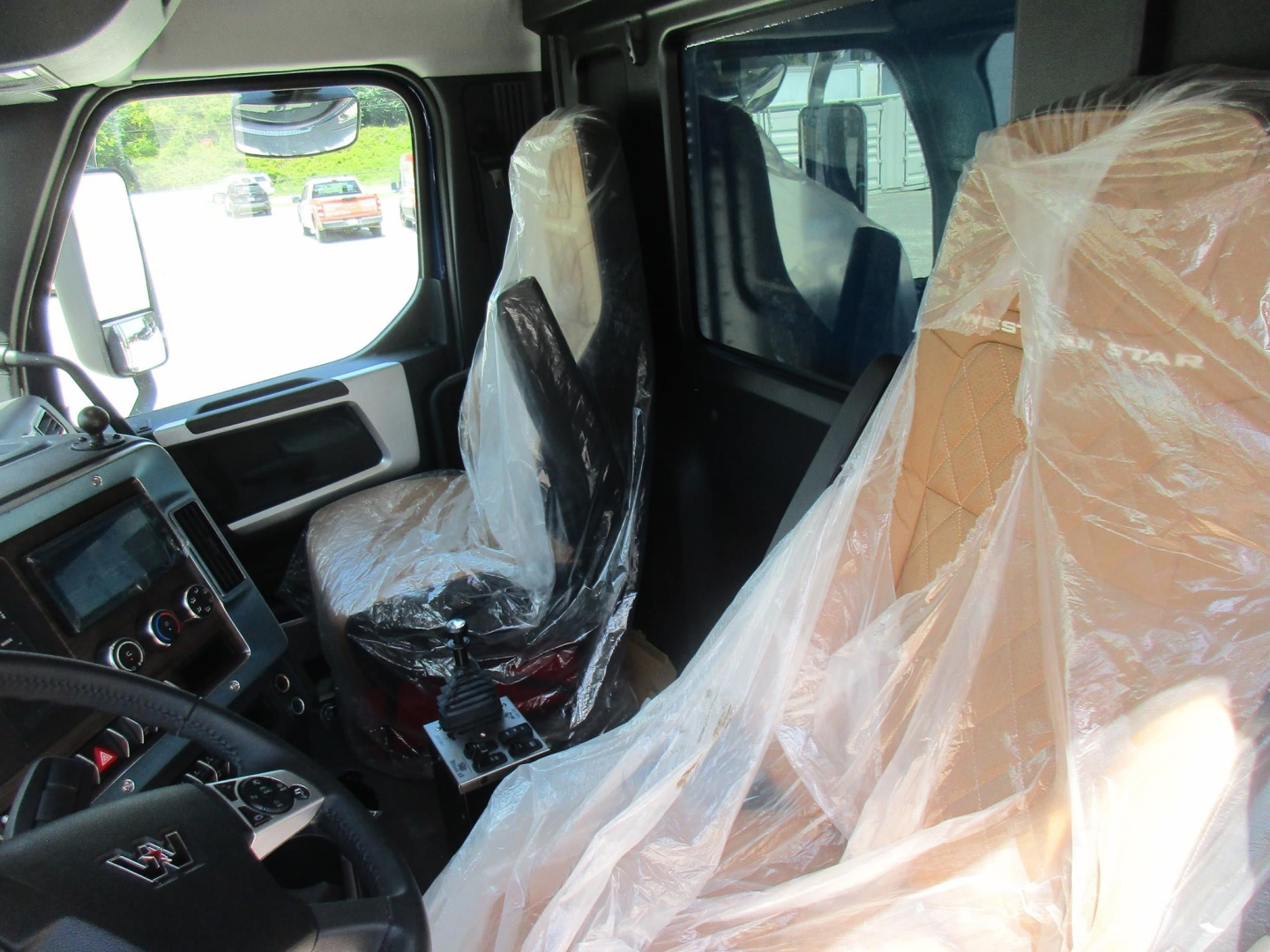 Truck cab interior of a Western Star 49X showing seats wrapped in plastic and dashboard area visible.