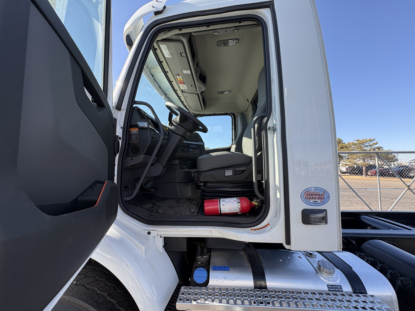 Volvo VHD64B300 cab interior view with open door; fire extinguisher mounted under dash; blue cap and metal steps visible on chassis; VIN and stock info not visible in text
