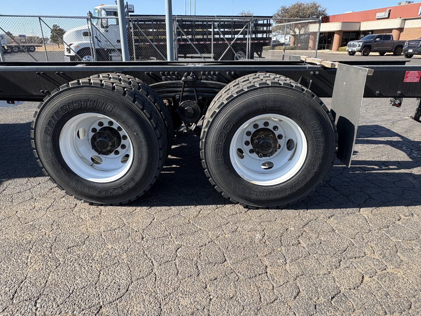Dual rear wheels with off-road tires on a flatbed trailer chassis, frame rails, and leaf spring suspension visible.