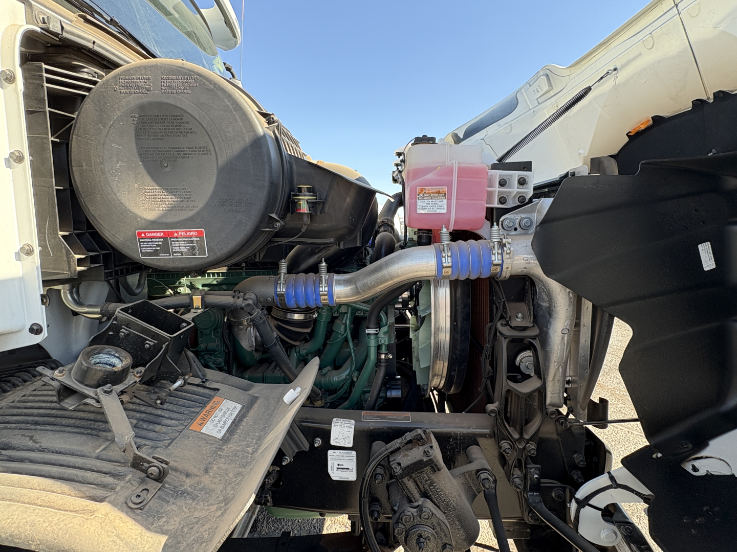 Volvo VHD64B300 truck engine bay showing coolant reservoir, air intake, and turbo piping facing a staggered engine layout.