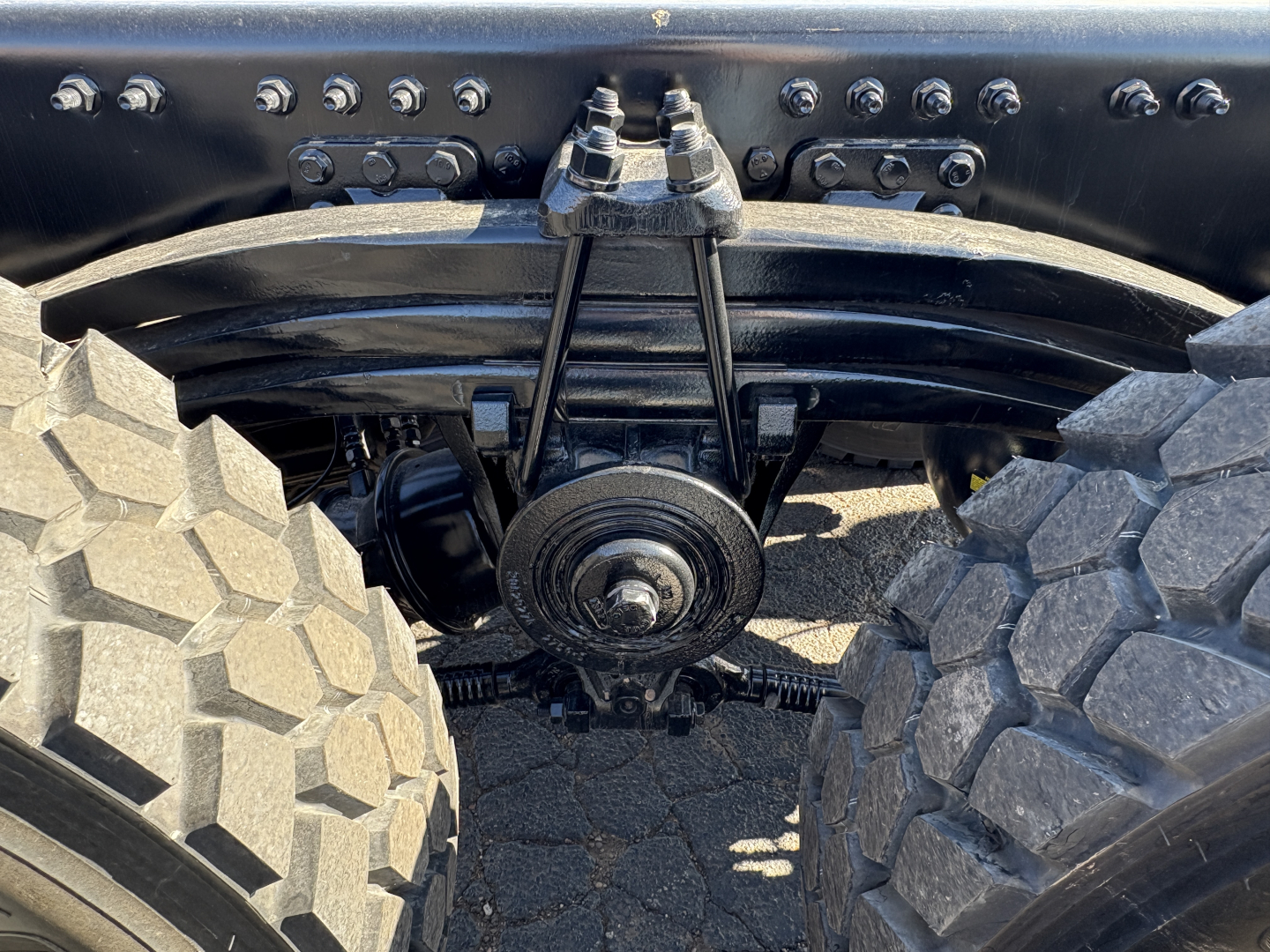 Vehicle rear axle area showing solid rear suspension with Dana/drive components, heavy-duty leaf springs and differential housing between large off-road tires.