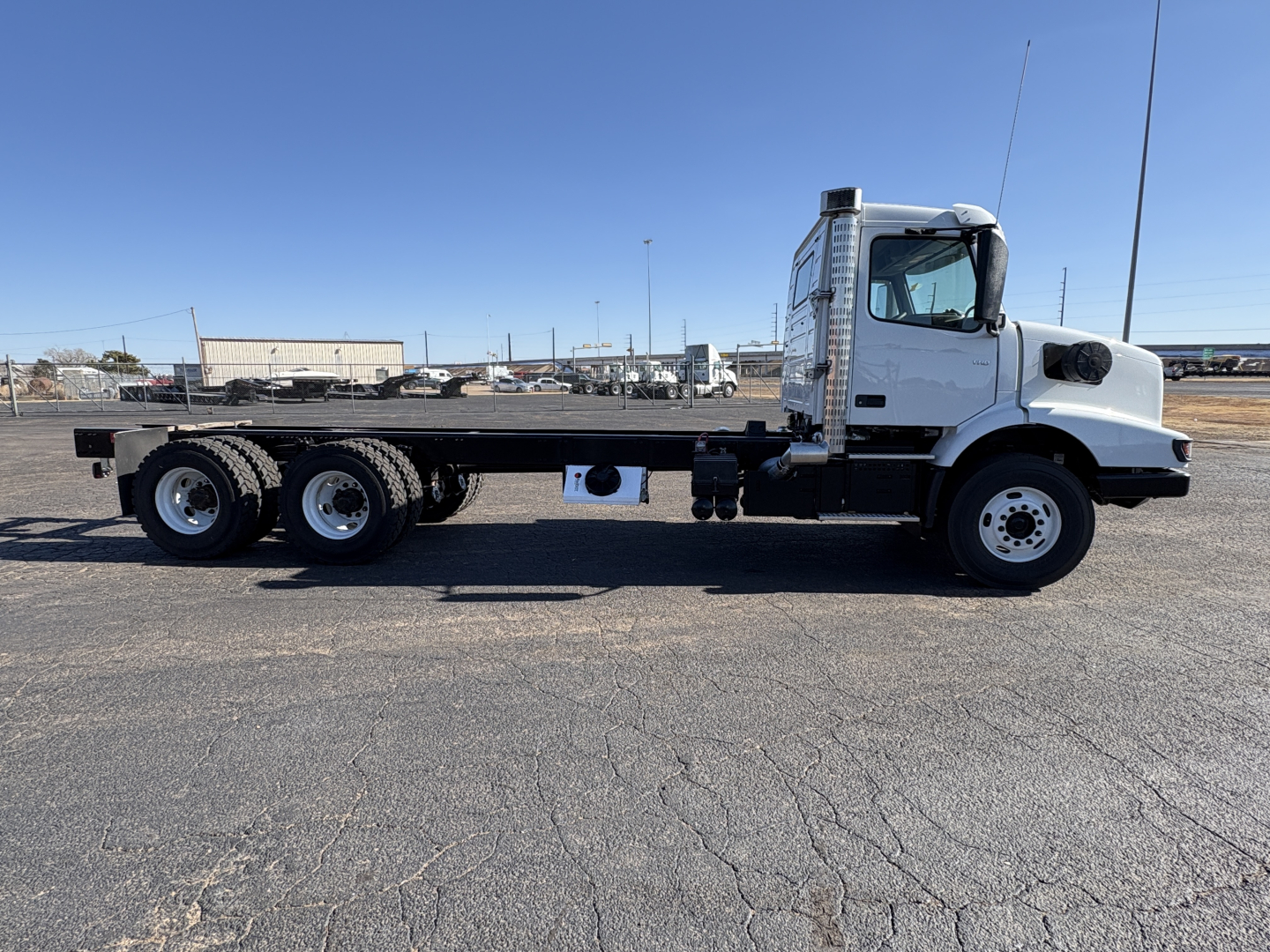 Side view of a white Volvo VHD64B300 heavy-duty truck on a flatbed chassis, showcasing the long wheelbase, dual rear axles, and cab with side exhaust.