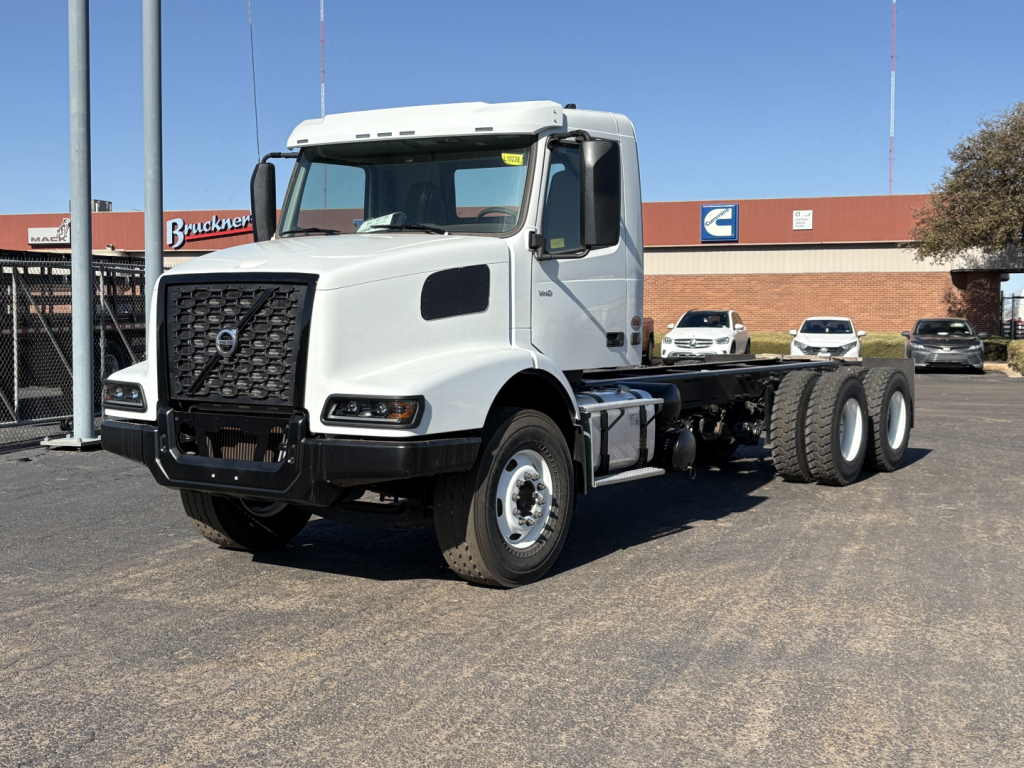 Volvo VHD64B300 tractor truck in white, two-axle cab with dual rear axles, front grille with Volvo emblem, side mirrors, parked outdoors.