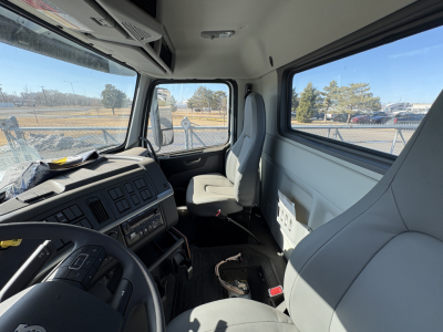 Truck cab interior showing driver's seat, dashboard, steering wheel, and passenger seat with gray upholstery in Volvo VHD64B300 cabin.