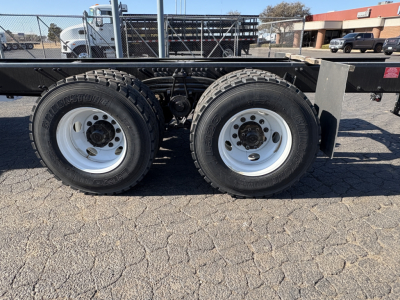 Dual rear wheels with off-road tires on a flatbed trailer chassis, frame rails, and leaf spring suspension visible.