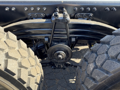 Vehicle rear axle area showing solid rear suspension with Dana/drive components, heavy-duty leaf springs and differential housing between large off-road tires.