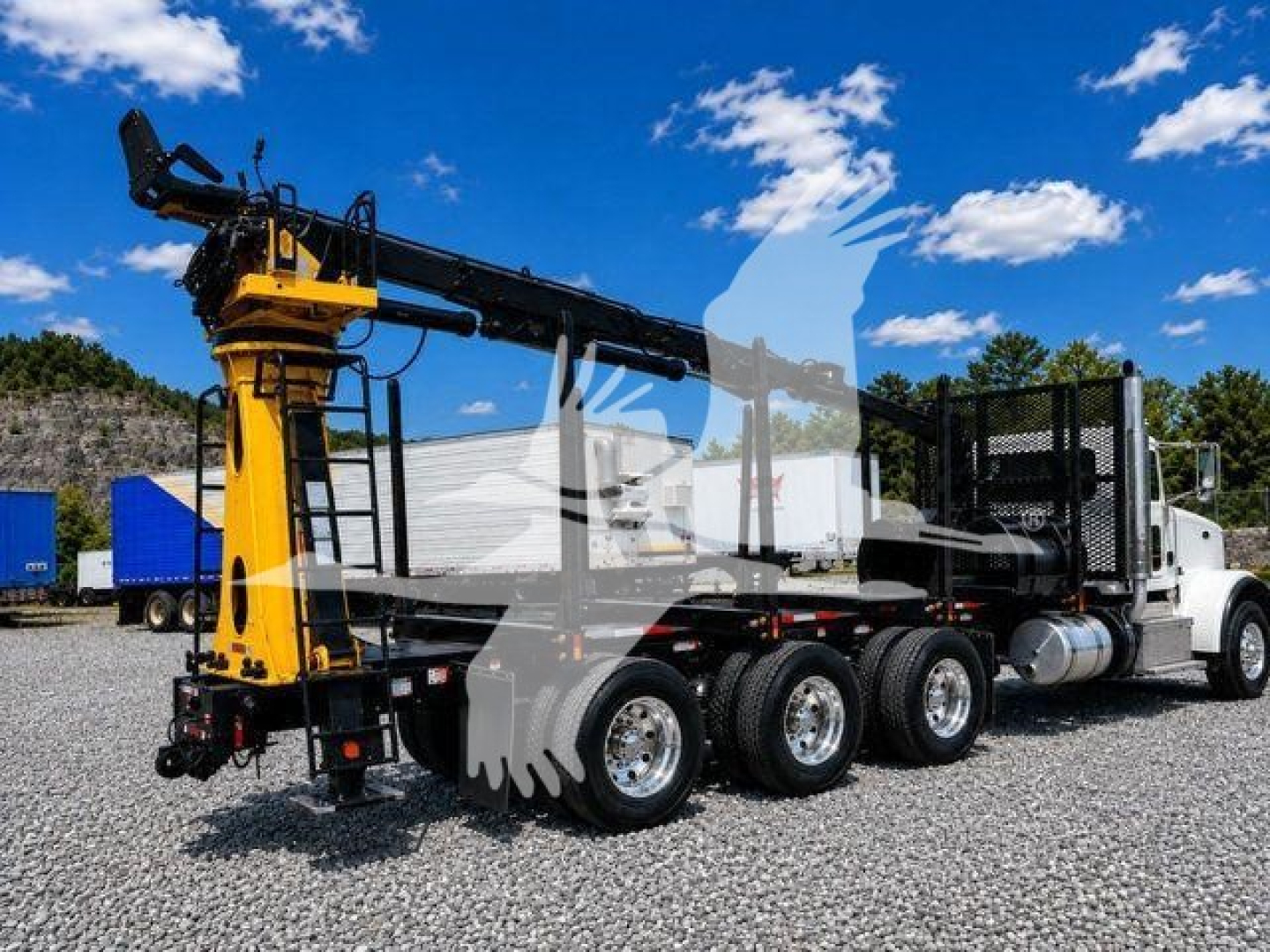 Peterbilt 367 grapple truck in service showing long boom and hydraulic arms with grapple at front, white cab, black chassis, multiple rear axles, gravel lot.