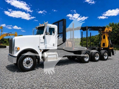 2016 Peterbilt 367 semi-tractor with white cab and black grapple trailer, side view showing triple rear axles and heavy-duty equipment in background.